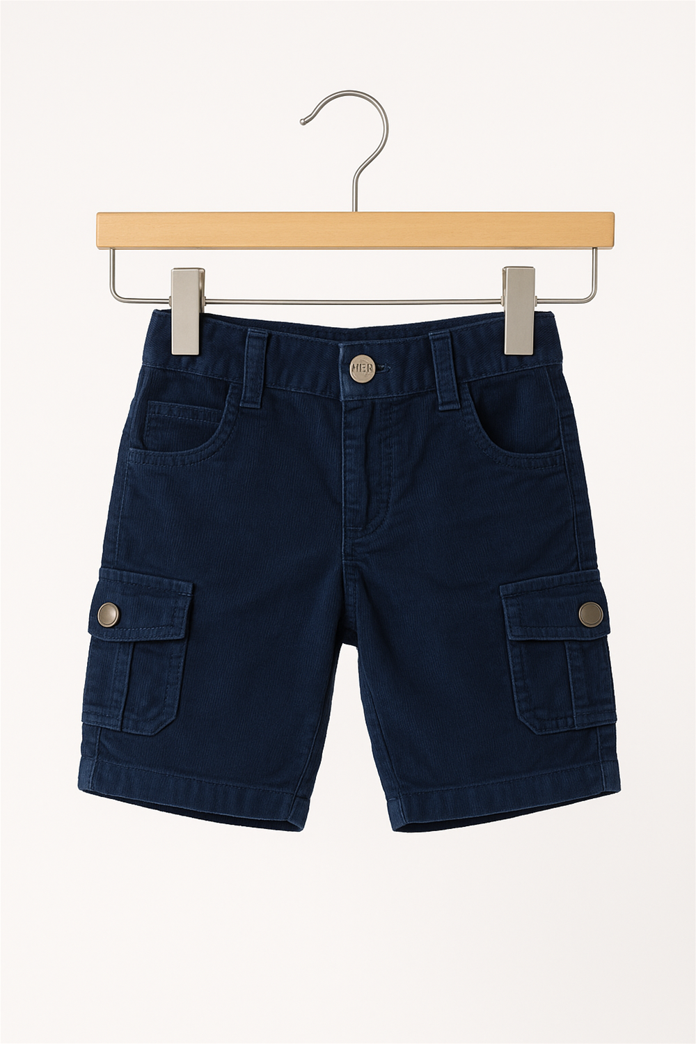 A pair of navy blue corduroy cargo shorts for children displayed on a wooden hanger. The shorts feature a metal button closure, belt loops, front and back pockets, and side flap cargo pockets with metallic snap buttons. The background is a plain off-white.