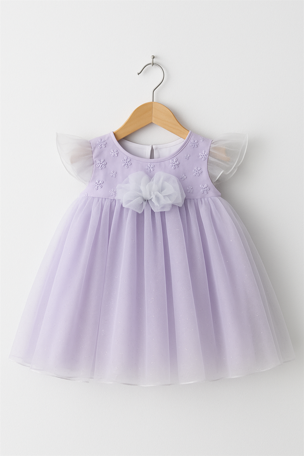 Lavender baby dress with floral embroidery and tulle skirt hanging on wooden hanger, featuring delicate flutter sleeves and organza bow.