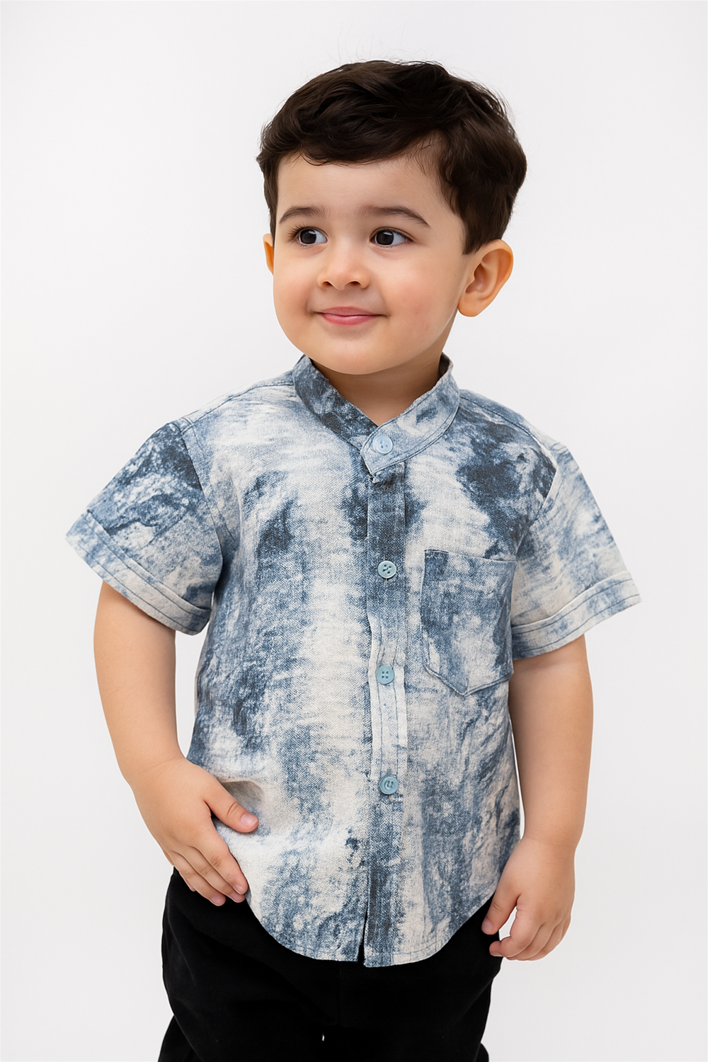 A young boy wearing a half-sleeve tie-dye type of design shirt with a normal collar, smiling side wise at the camera.