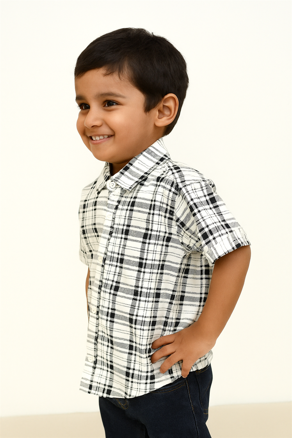 A young boy wearing a Black and white half-sleeve shirt and jeans, smiling while standing outdoors.