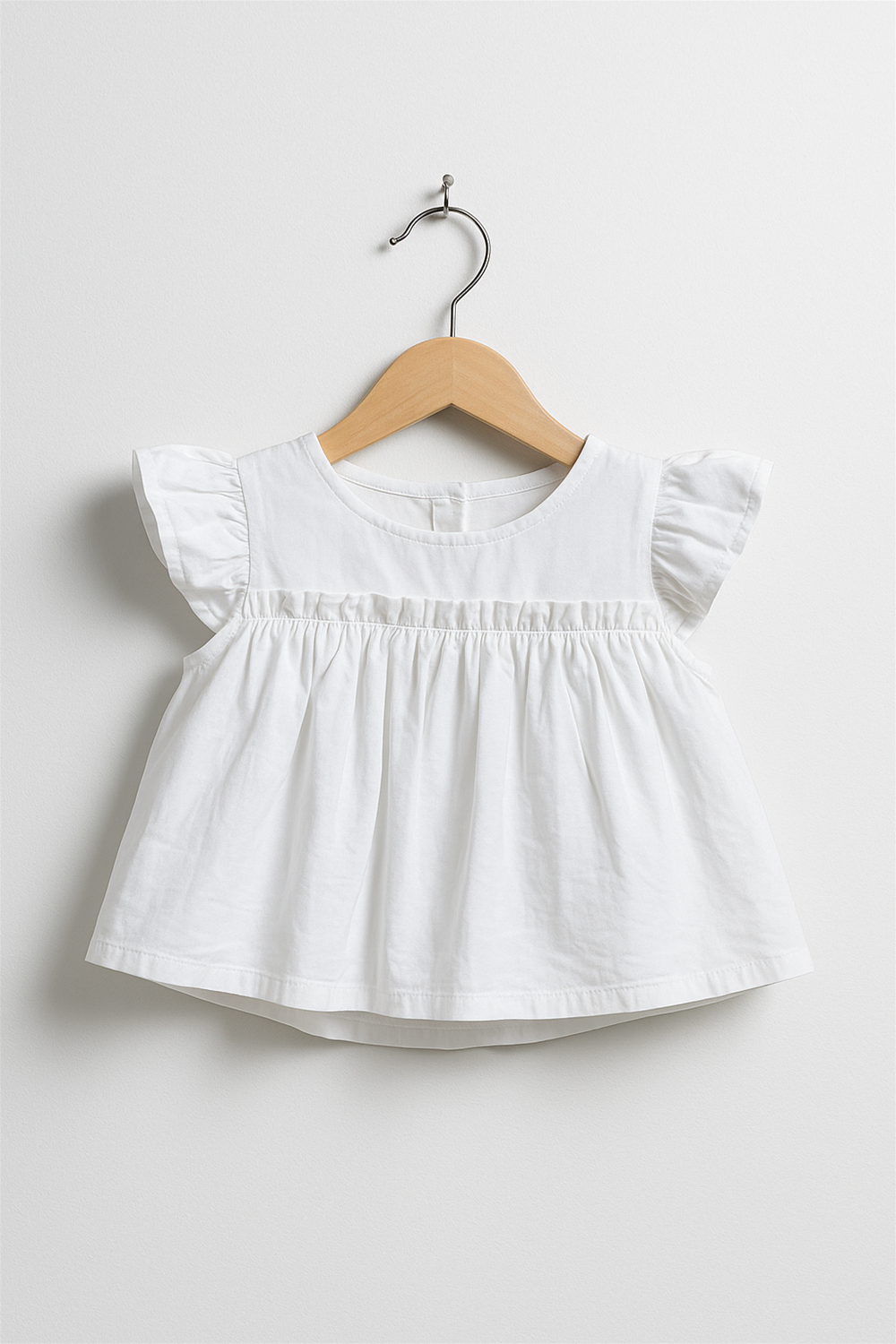 A white baby top on a wooden hanger with flutter sleeves and gathered pleats, designed for casual summer wear.