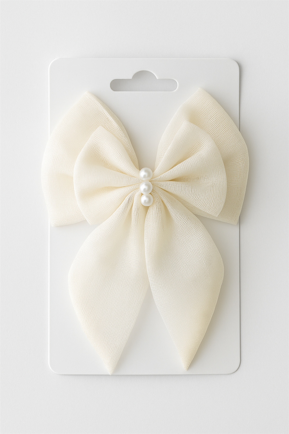 Cream-colored bow hair accessory with pearl centerpiece, neatly attached to product card, presented against a clean white background for retail.