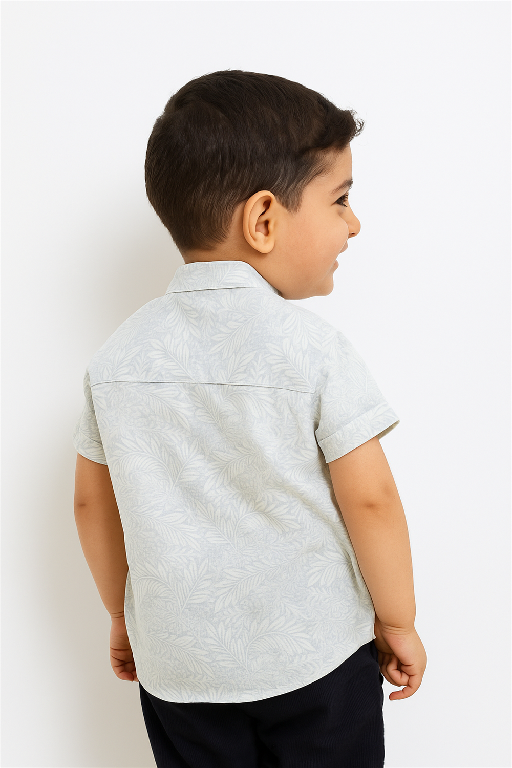 A young boy is seen from the back wearing a half-sleeve Chinese collar shirt in soft grey with a subtle leafy print. The shirt showcases a clean yoke seam and rolled sleeves, offering a stylish and comfortable design.