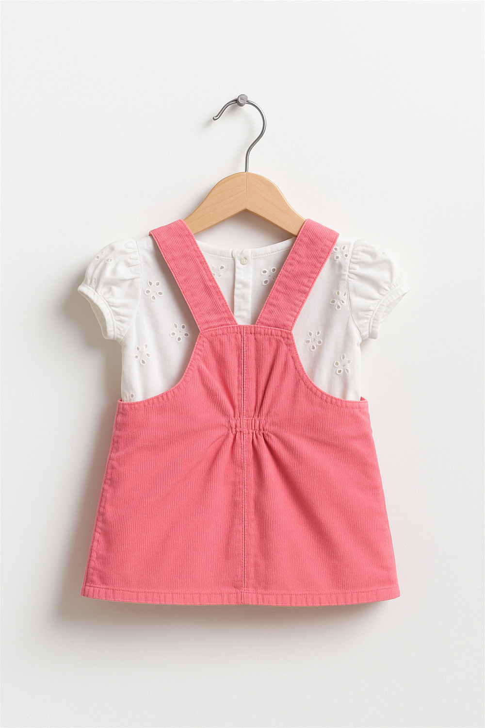 A pink corduroy pinafore dress in hanger back view.