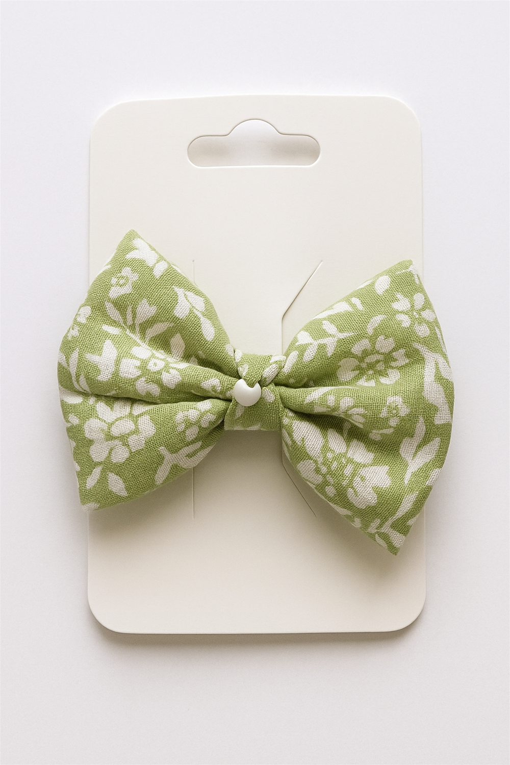 Green floral bow hair clip with pearl center, attached to cream display card, showcasing product packaging for retail presentation.