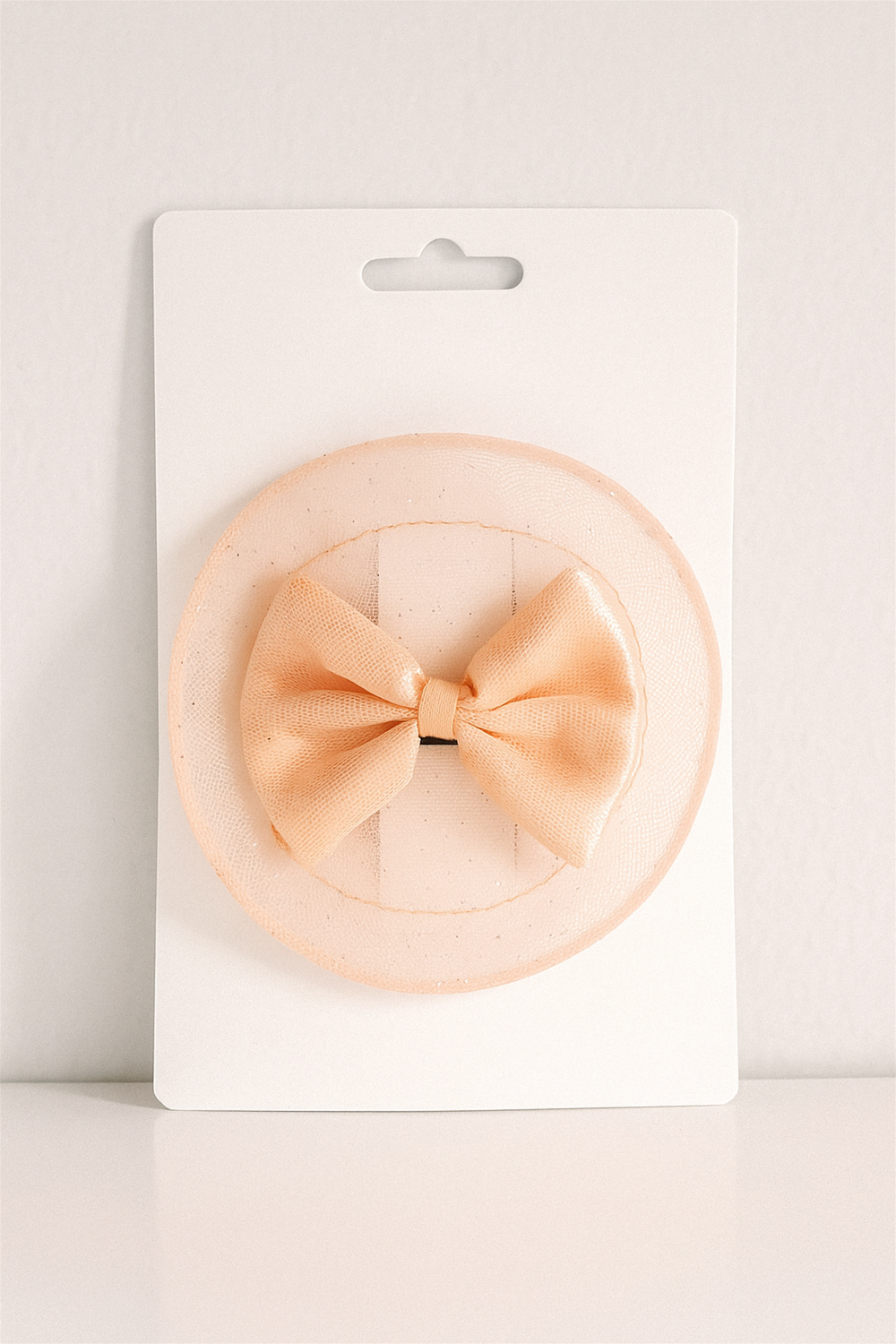 Peach bow hair clip displayed on white card packaging with circular netted layer, designed for elegant baby accessory presentation.