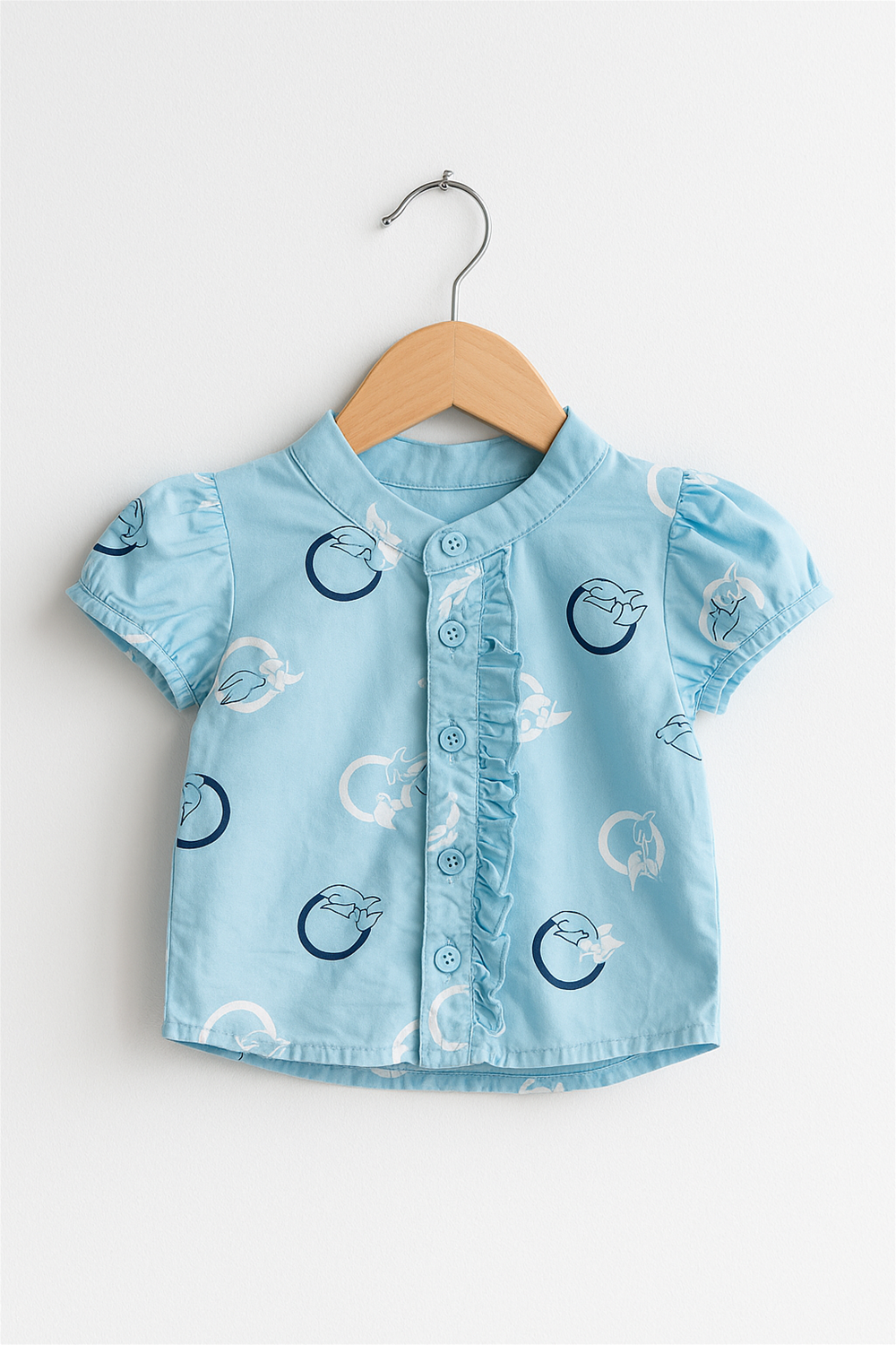 Light blue girls’ top on wooden hanger, Chinese collar, puff sleeves, ruffled button placket, circle bird print design.