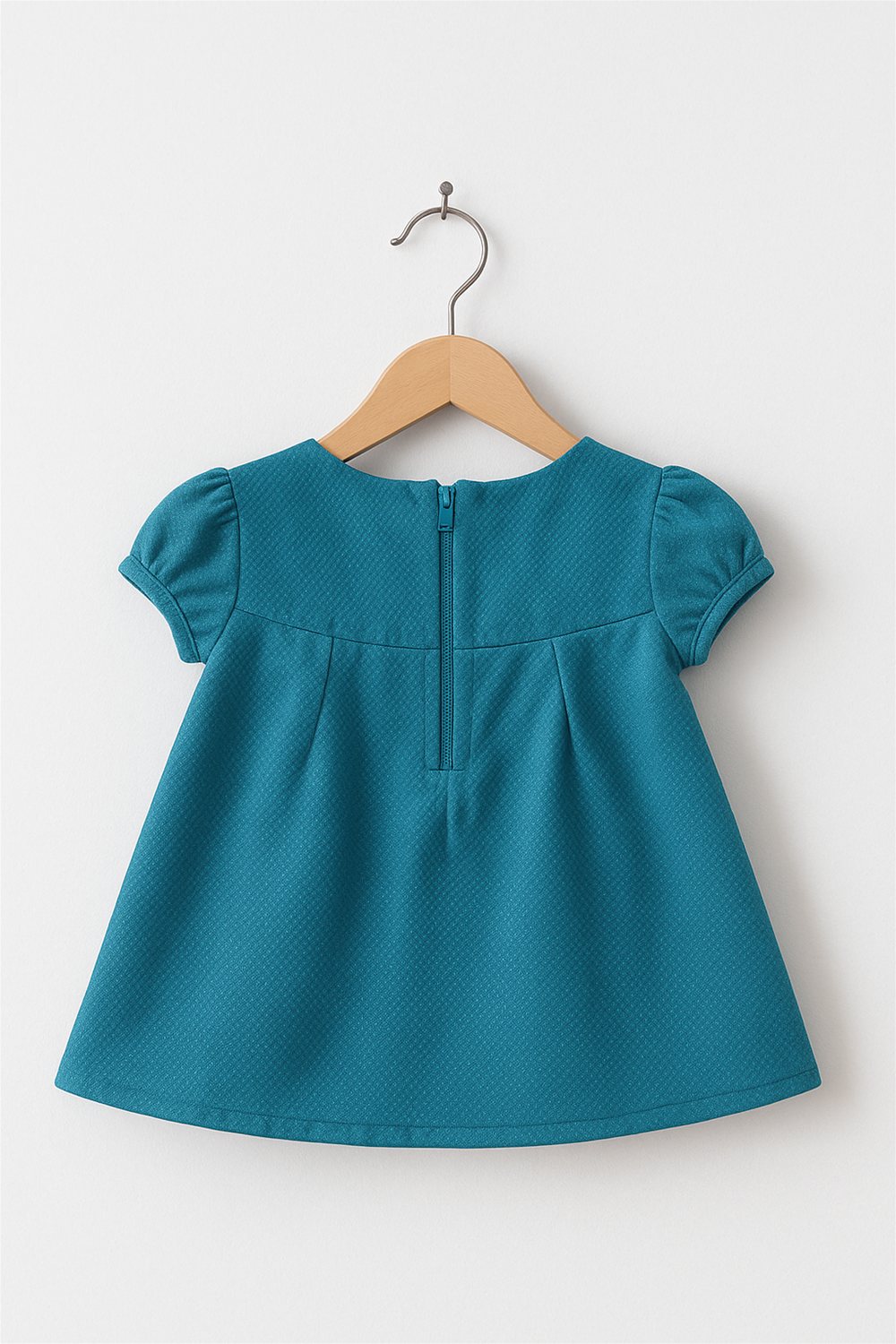 A peacock blue dress in zil mil material hanging in a wooden hanger back view.