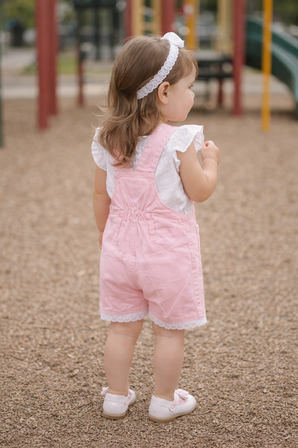 Toddler wearing pink dungaree from behind, paired with white top.