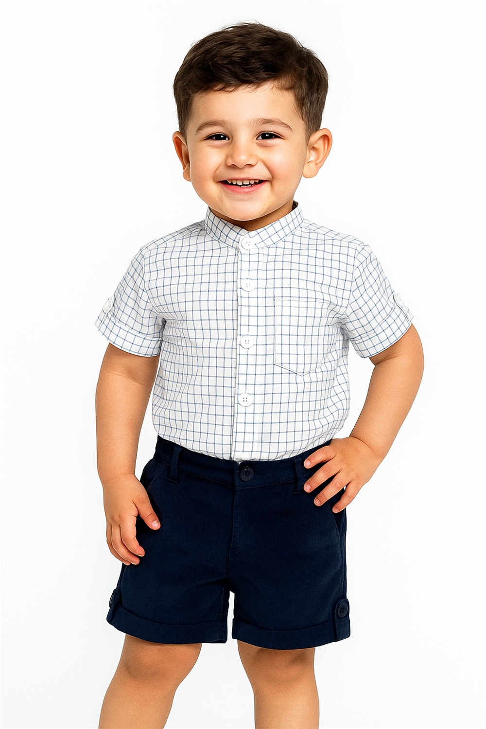 Smiling toddler in white checkered shirt and navy shorts, hands on waist, posing confidently in bright studio light.